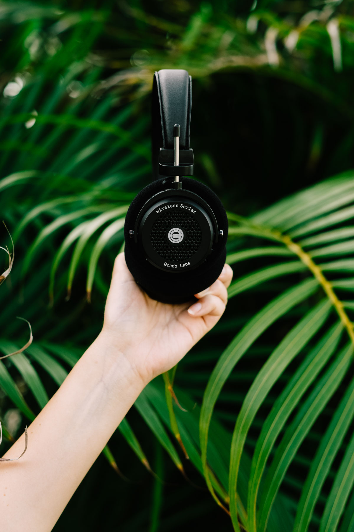 Photo of GW100 headphones being held in front of large green leaves