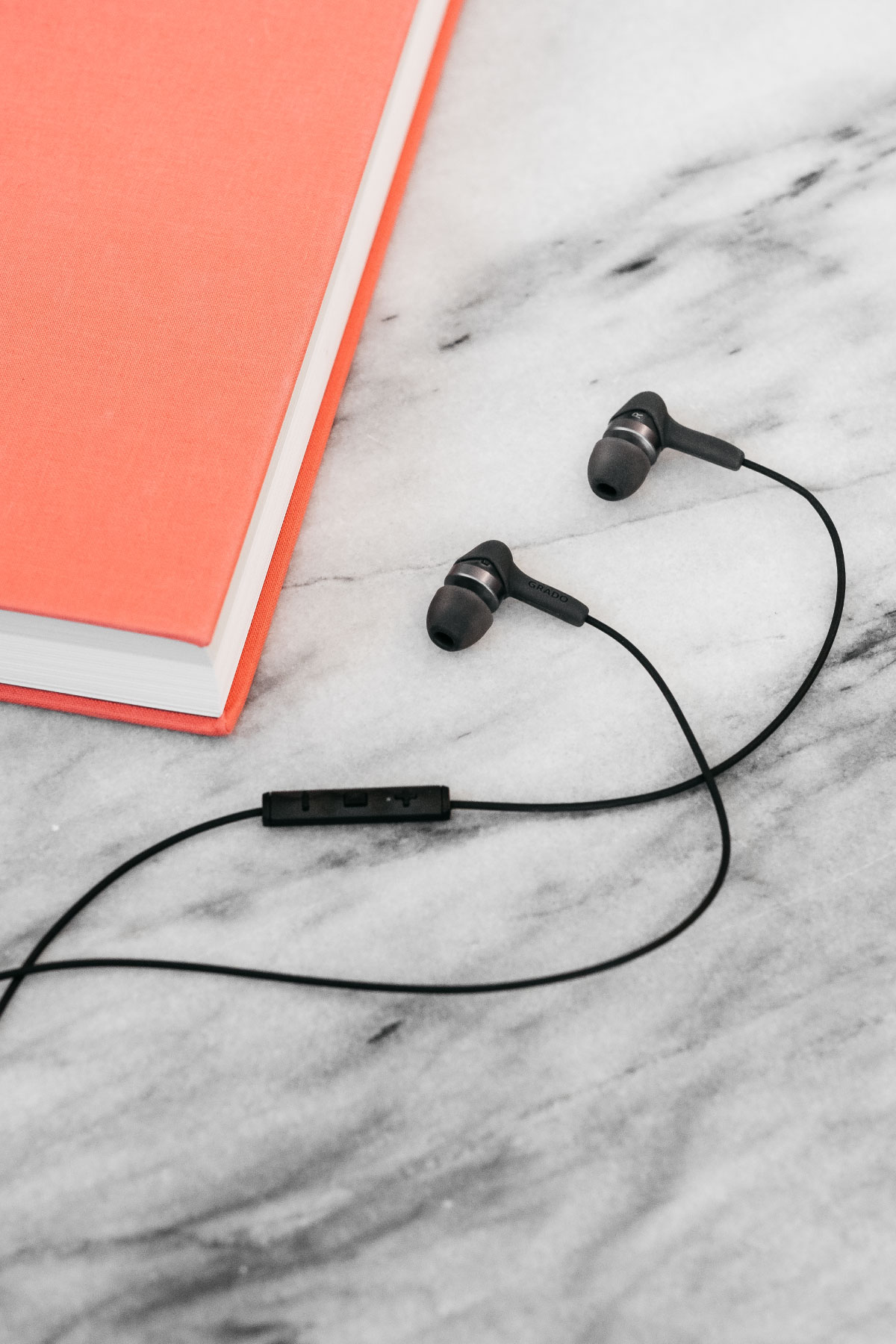 Photo of Grado ige3 headphones laying on a white marble table next to a salmon colored book
